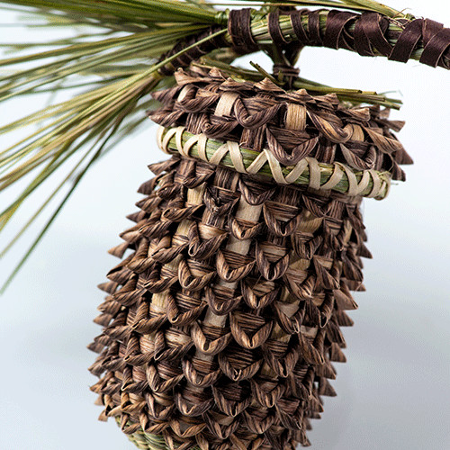 Detail of basket shaped like an acorn with pine needle decoration on cover.