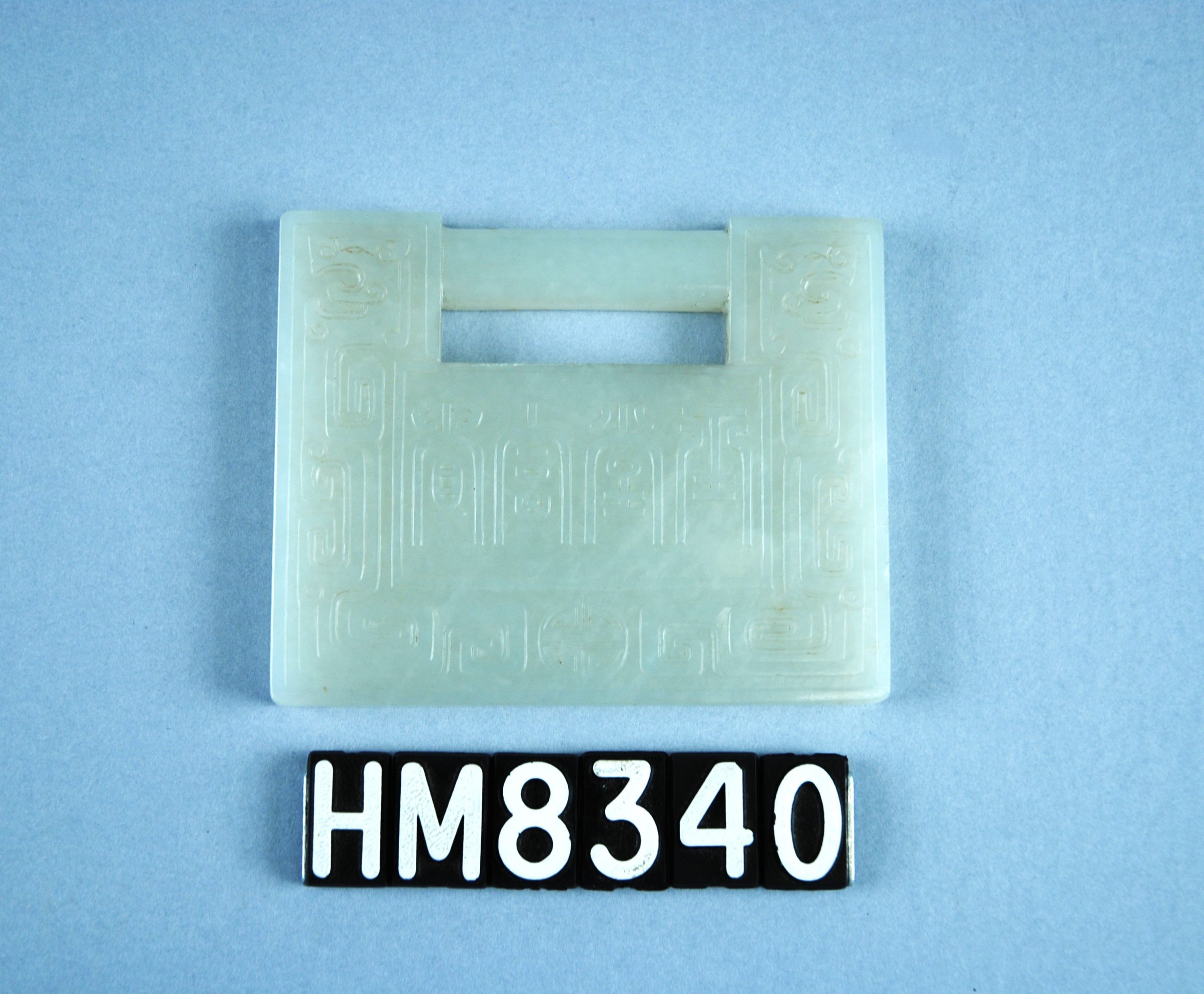 Image of small jade object, rectangular in shape, with pierced handle hole at top and inscribed designs.