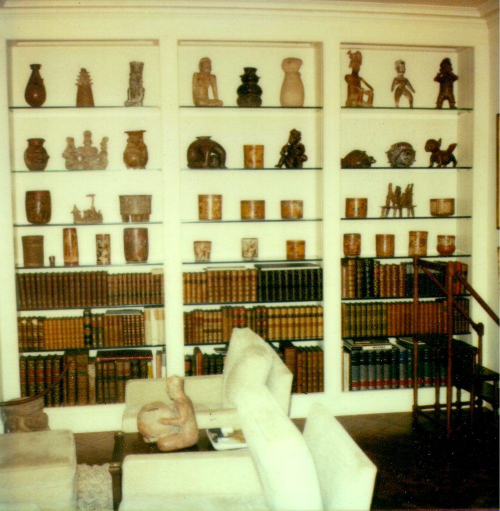 palmersm Image of a wall of built-in shelves behind furniture. The bottom shelves hold books, the upper shelves hold a variety of ceramic objects.