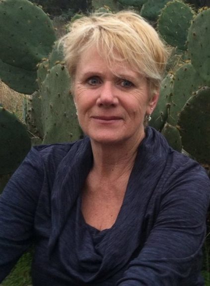 Image of Caucasian woman with short, blond hair sitting in front of a cactus.