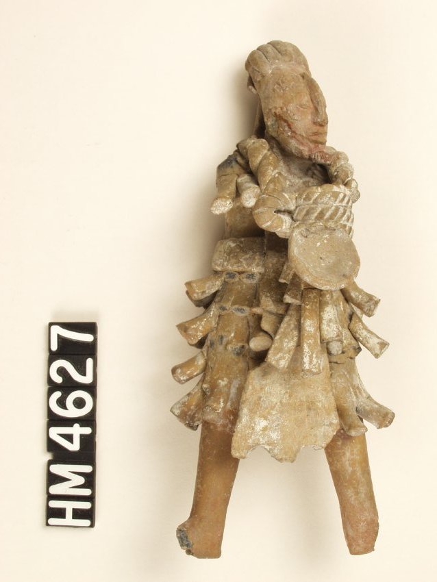 Very small ceramic figurine with spondylus shell ornament, an artificially modeled nose, and a deformed head with a sloping forehead. He also has marks representing facial scarification or painting. His clothing is tattered.