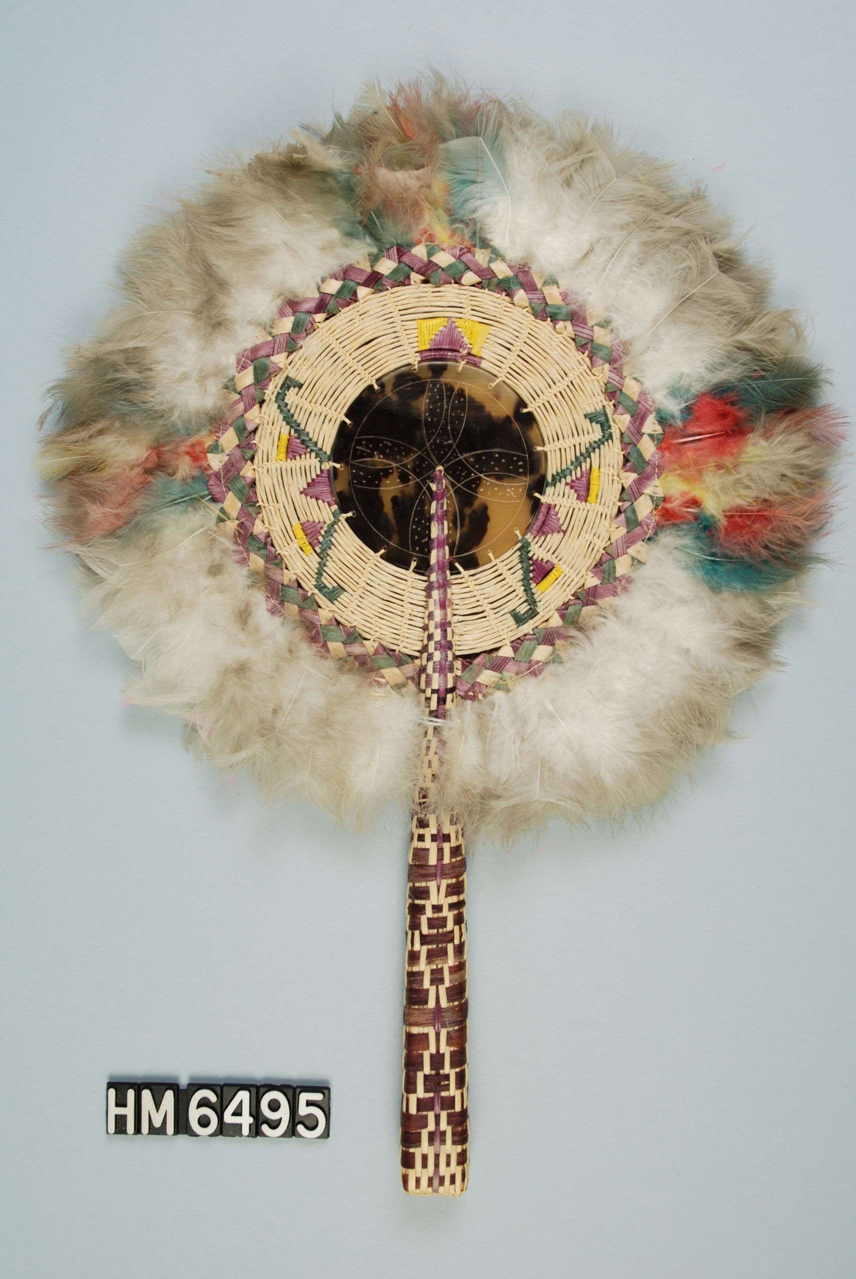 Image of a hand-held fan. Handle is woven, fan portion is circular with tortoiseshell at center surrounded by woven strips and finally feathers.