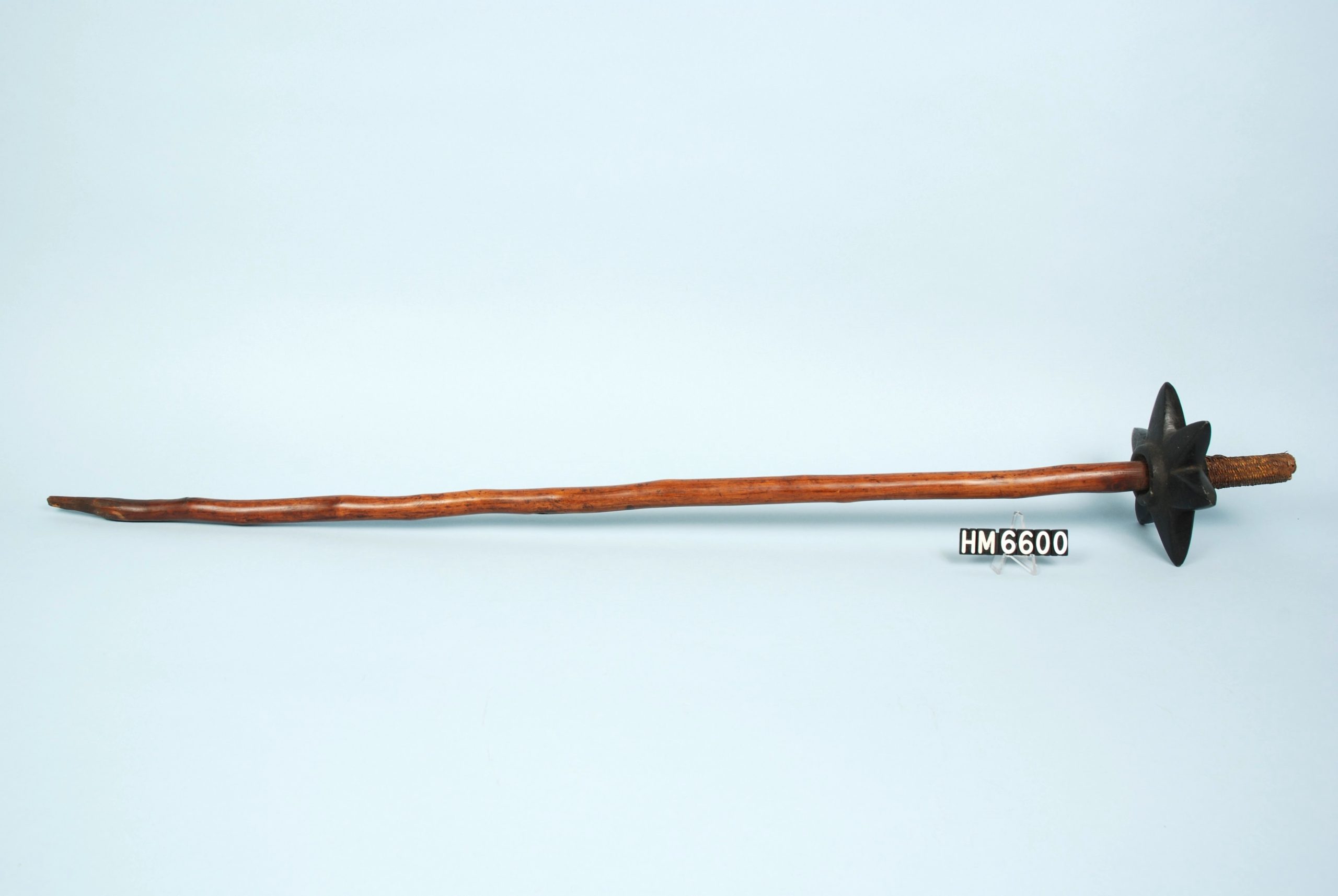 Image of a club made with a long stick, polished but retaining its natural shape, with a stone carved into a ring of points, attached a few inches below one end.