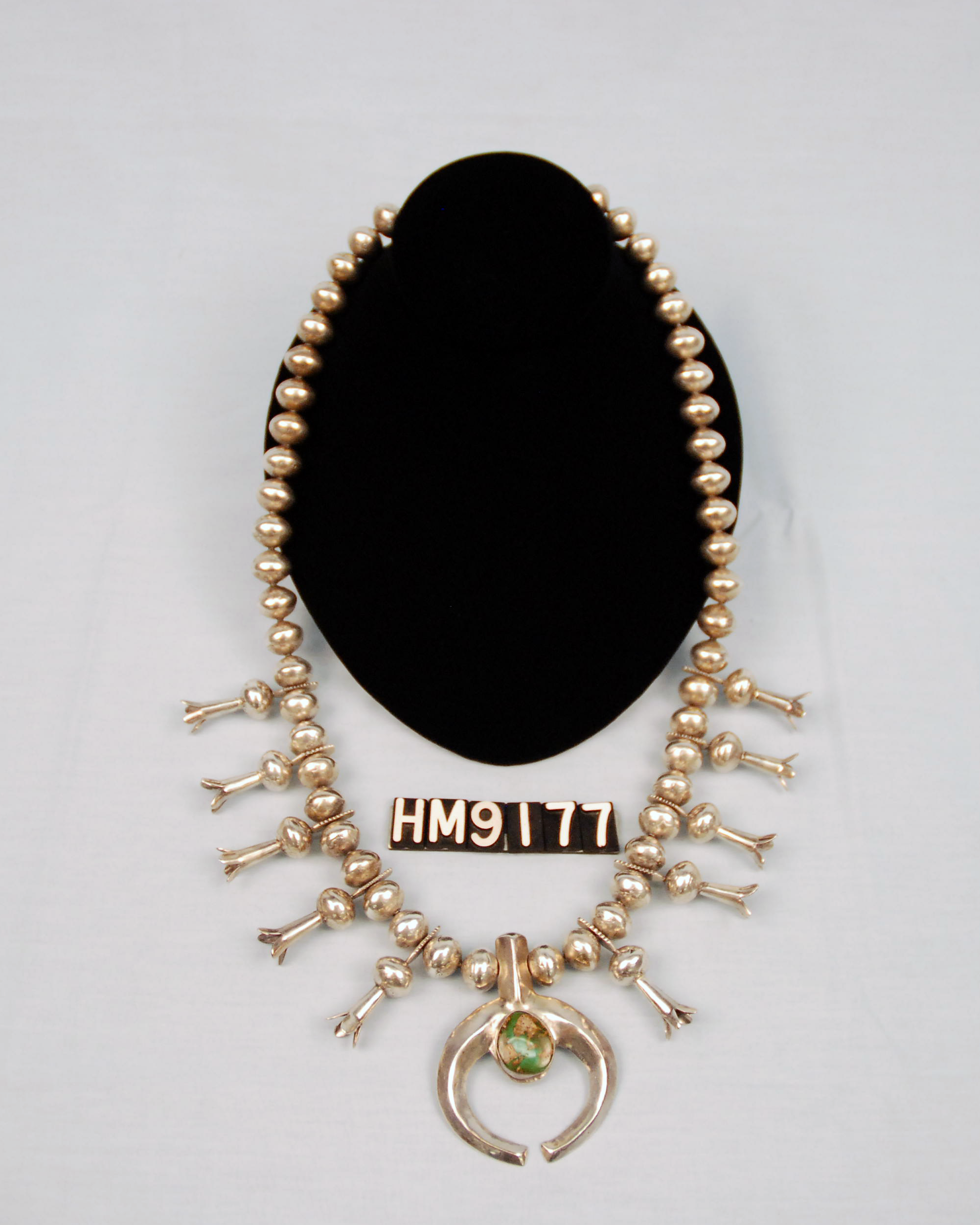 Image of a silver necklace with beads shaped like squash blossoms.