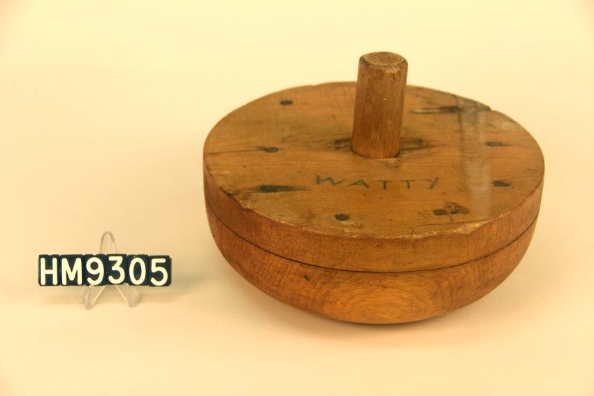 Image of basket block, circular and rounded toward base, with handle in center. "Watty" is inscribed on the top.