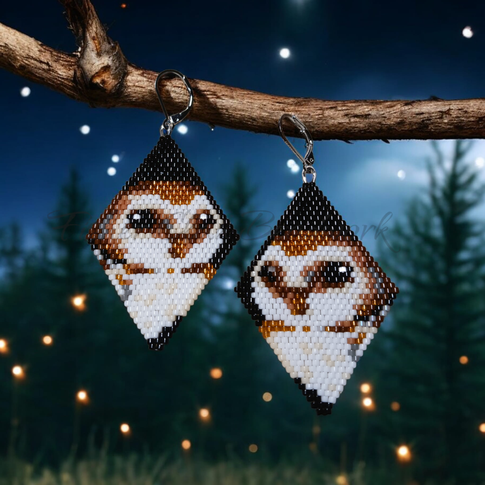 Image of earrings hanging from a stick in front of an image of fireflies and trees. The earrings are kite-shaped and have an owl motif.