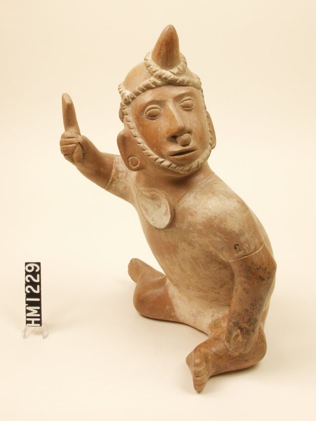 Seated ceramic figure with a throwing device in raised right hand, a pendant on neck, and a head ornament. Wears a nose ornament and headdress.