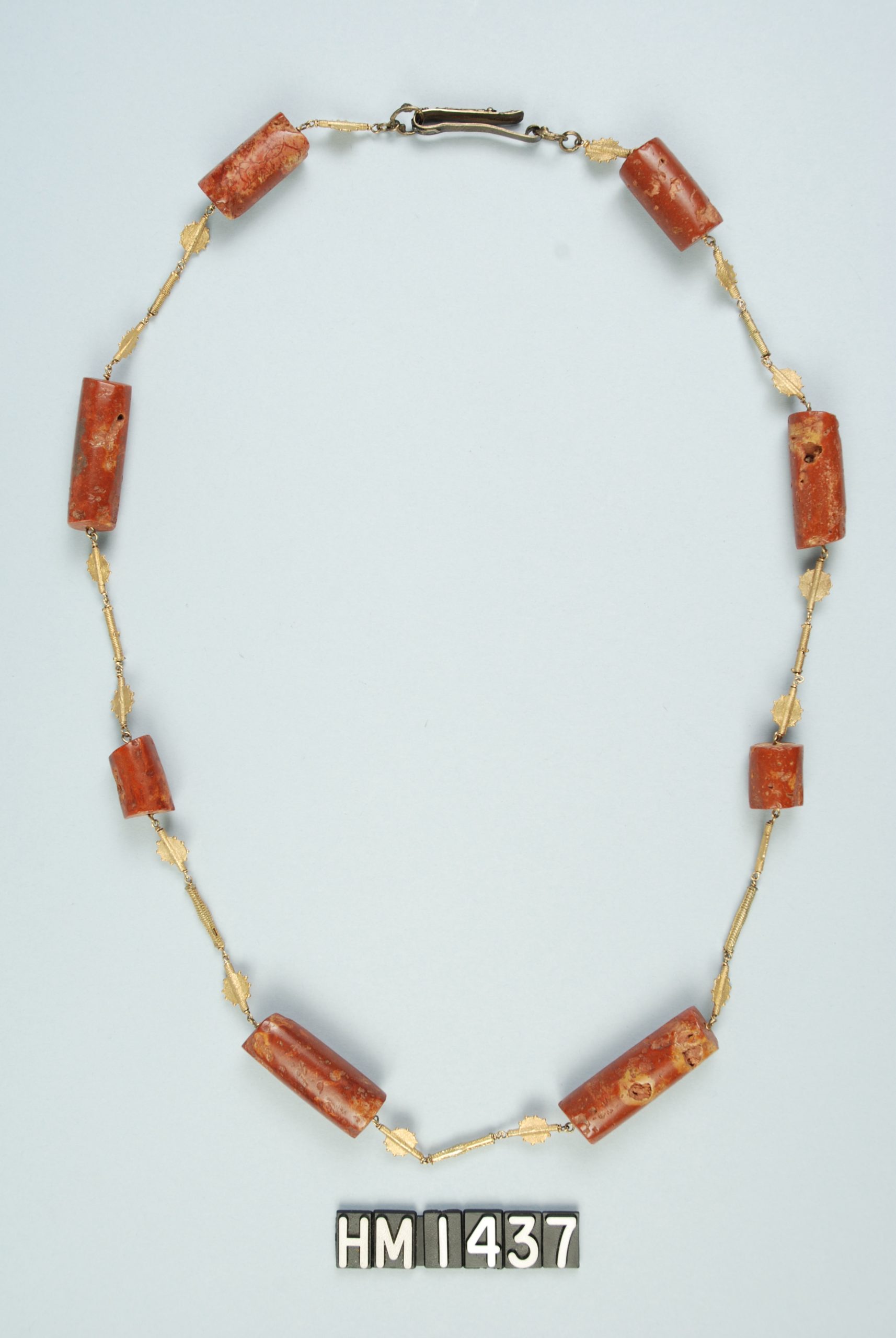 Image of necklace with decorative gold links and carved red stone elements.