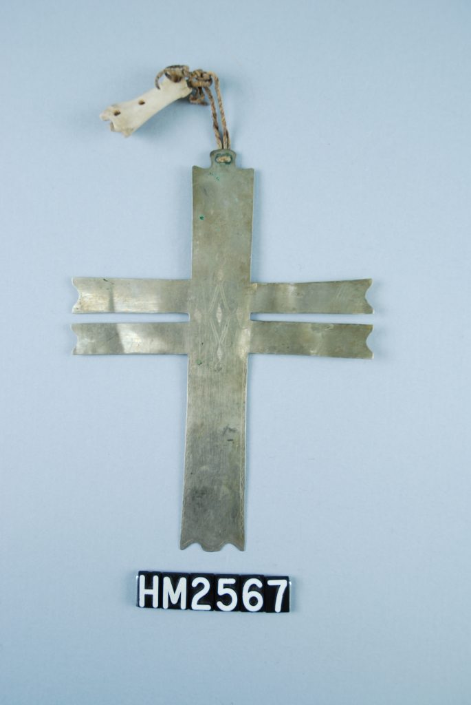 Image of a silver ornament shaped like a cross with a double cross-piece and a bone element attached at top.
