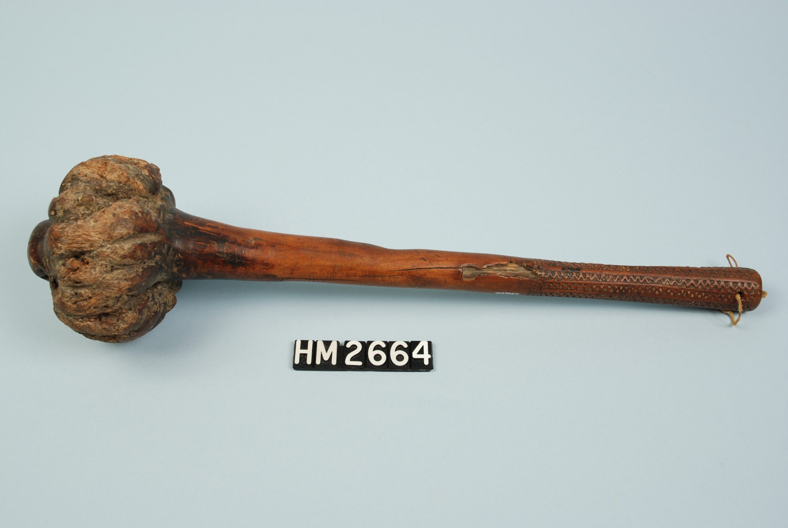 Image of short club made of a single piece of wood. Handle has chip-carved patterns at the grip. Head is formed of large burl.