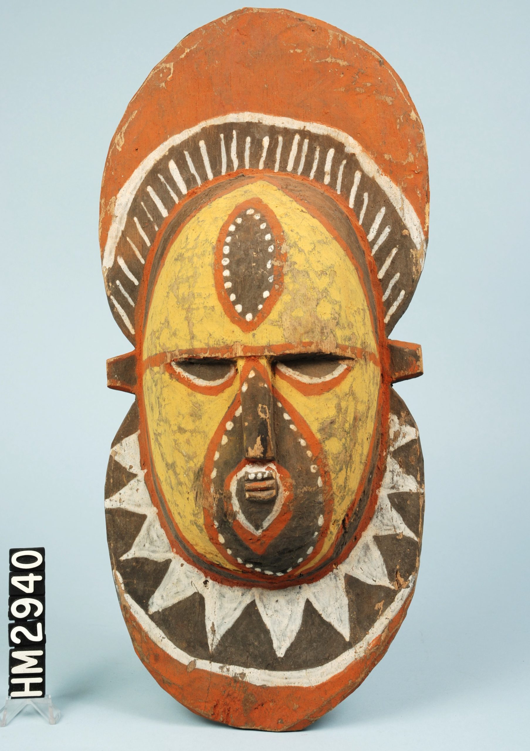 Image of painted wooden mask in yellow, brown, white, and orange.