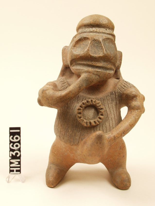 Small ceramic figure wearing headdress with band of vertical incised stripes. Face is skull-like: large indented eyes and nose, indented wide mouth. One arm flexed with hand up to mouth, the other arm bent with hand on phallus which is large and erect. Shirt has incised vertical lines and a protruding circle with incised lines radiating from center. Four bumps on each upper arm, hands not modeled. Legs short.