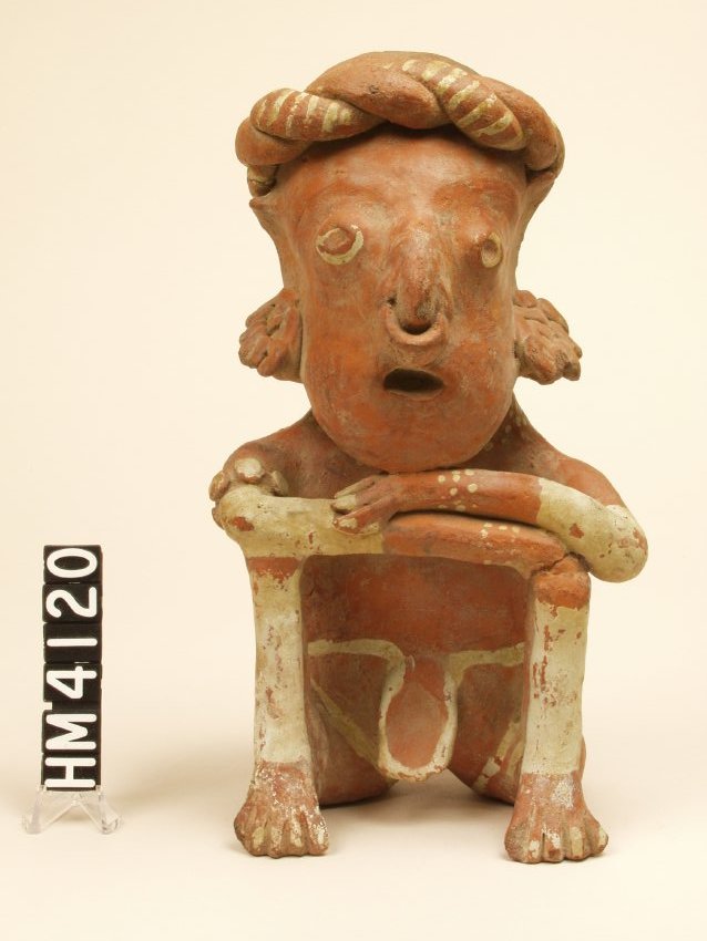 Ceramic figure seated with both legs bent and drawn up to chest; feet flat on the ground. Arms are crossed and rest on knees.