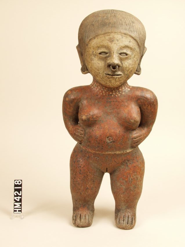 Standing ceramic figure of a female, unclothed, with hands on hips.