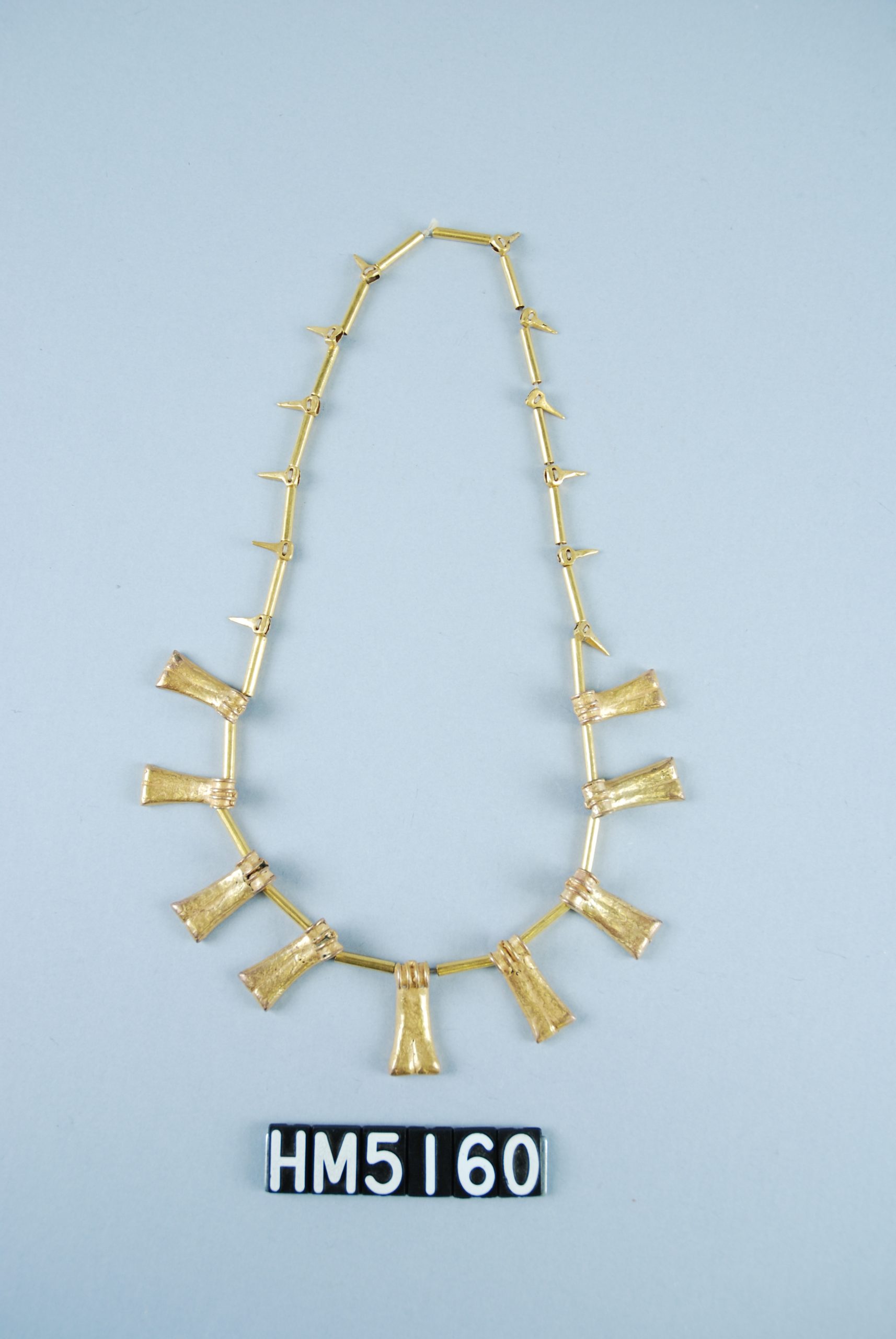 Image of necklace made with gold beads shaped as tubes, shaped as small pointed elements, and shaped as finger bones.