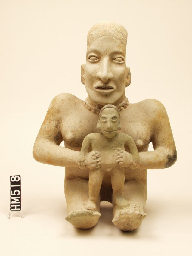 Ceramic mother and child figure. Hair indicated by detailed grooves. Female's chest still shows signs of elaborate black tattoo swirls and she wears a beaded necklace.