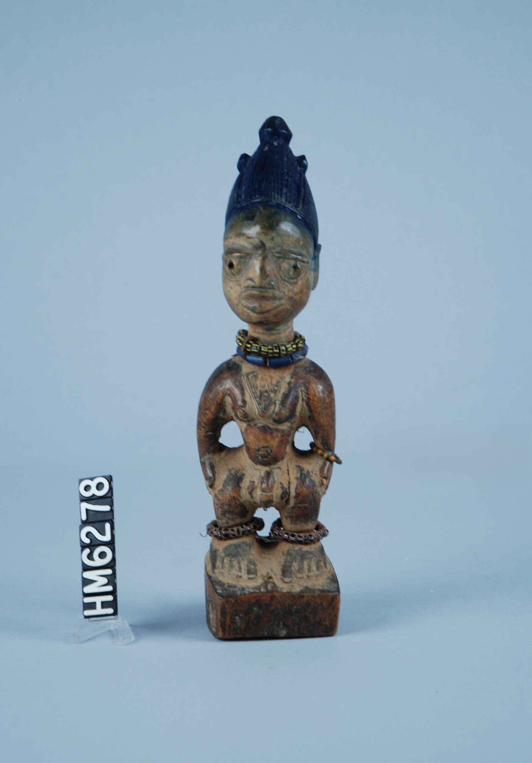 Image of a carved wooden figure with beaded jewelry and blue headdress.