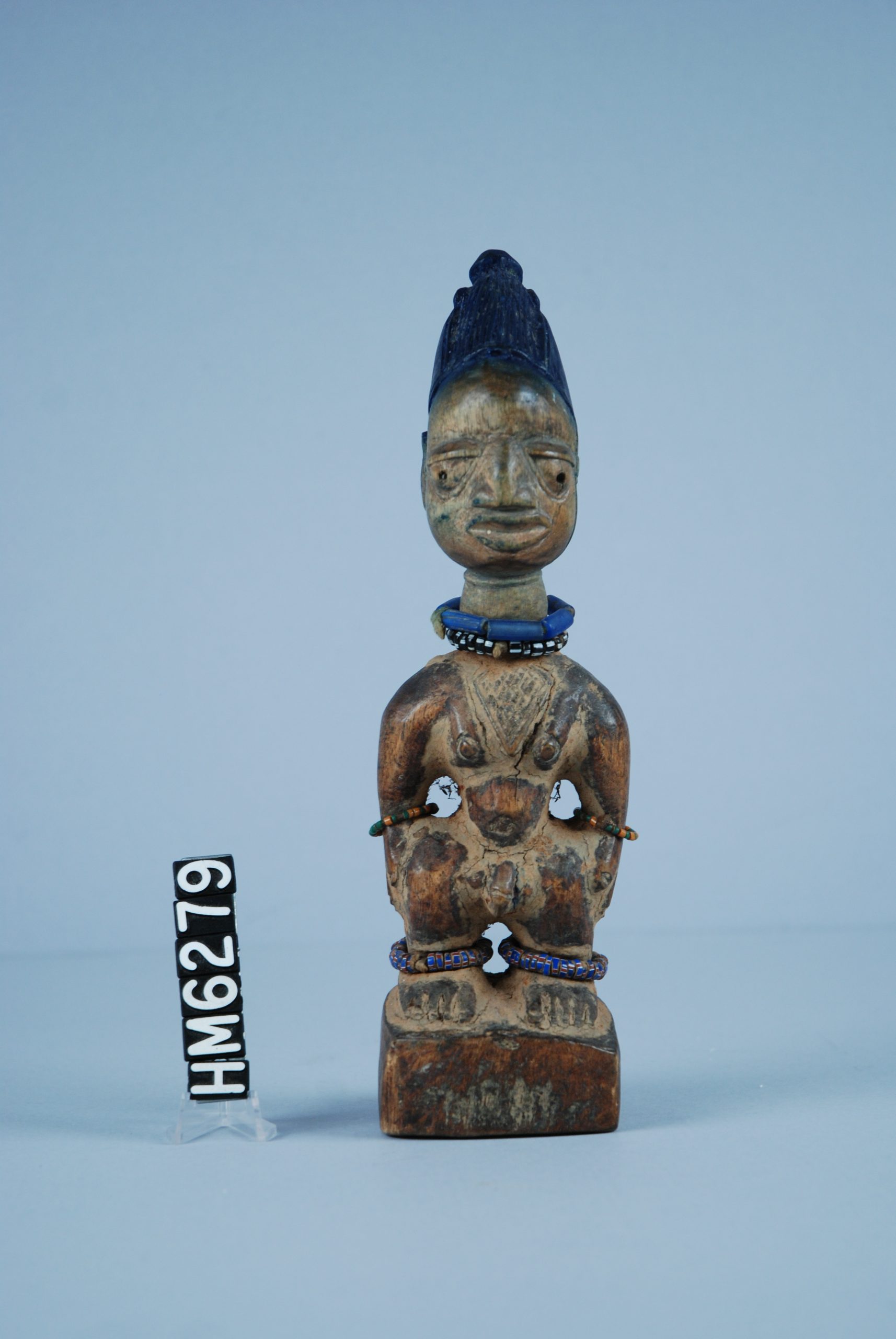 Image of a carved wooden figure with beaded jewelry and blue headdress.