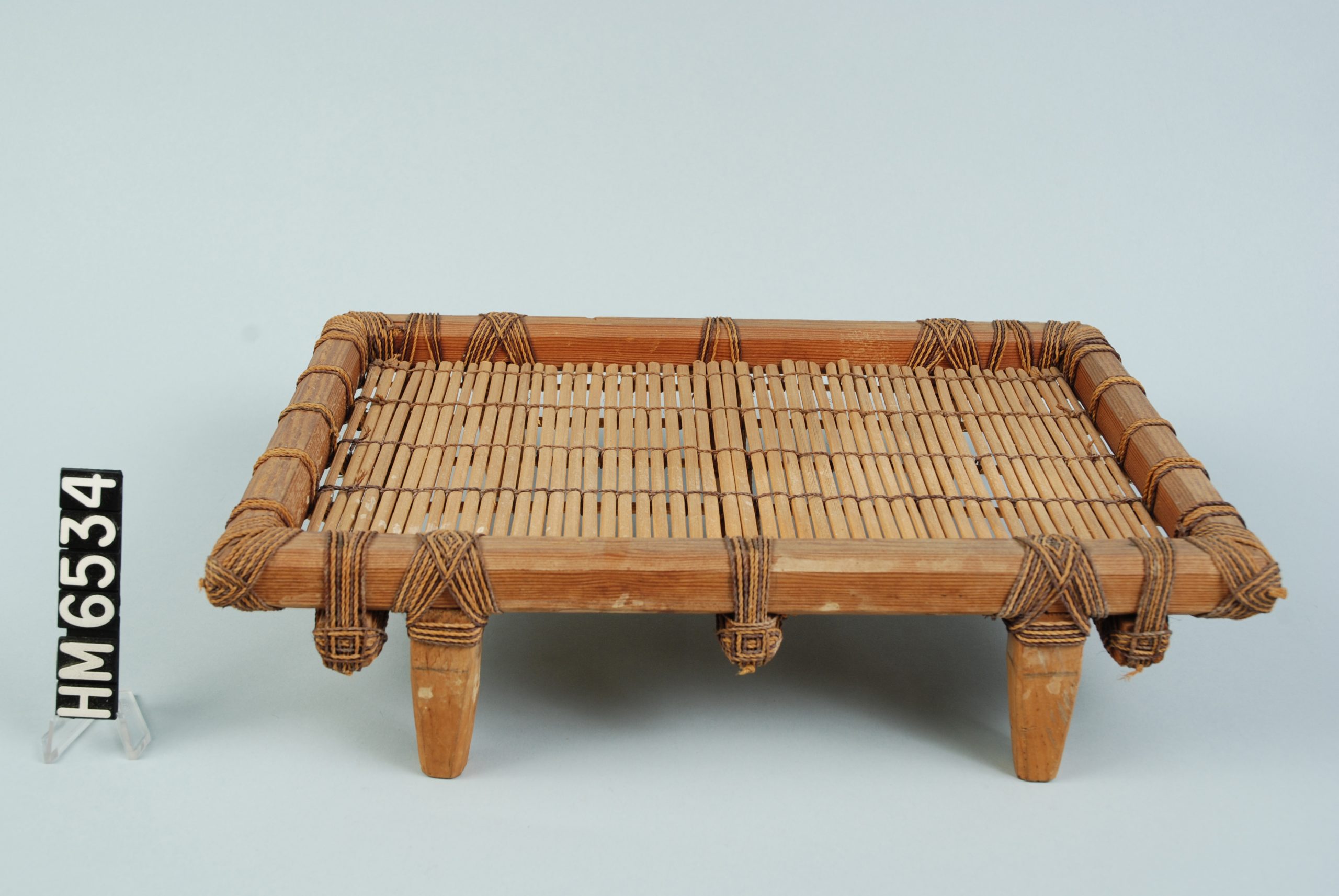 Image of object made as rectangular frame with four legs and holding a woven mat.
