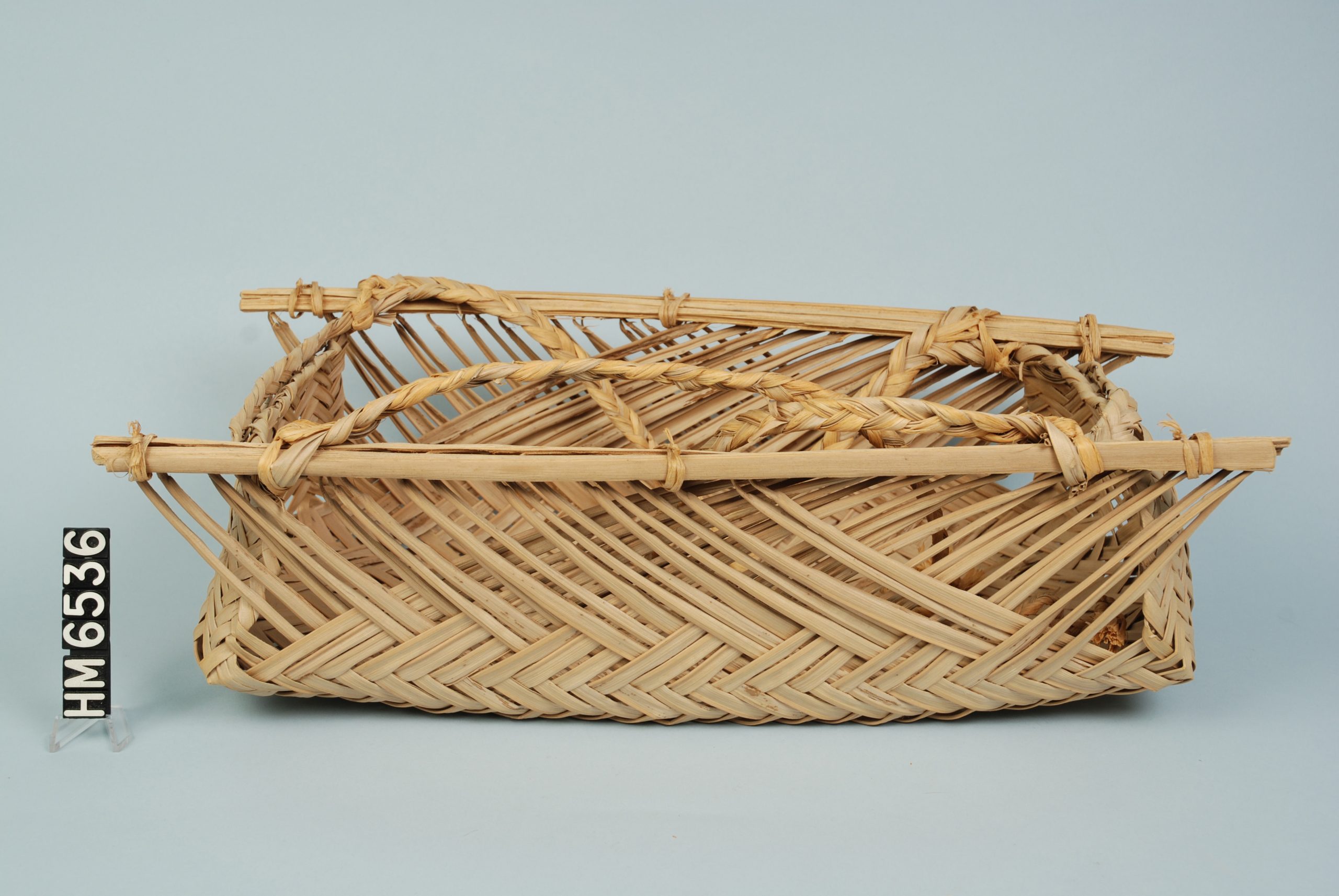 Image of a basket woven of reeds with bamboo forming a rim at two sides of the top.