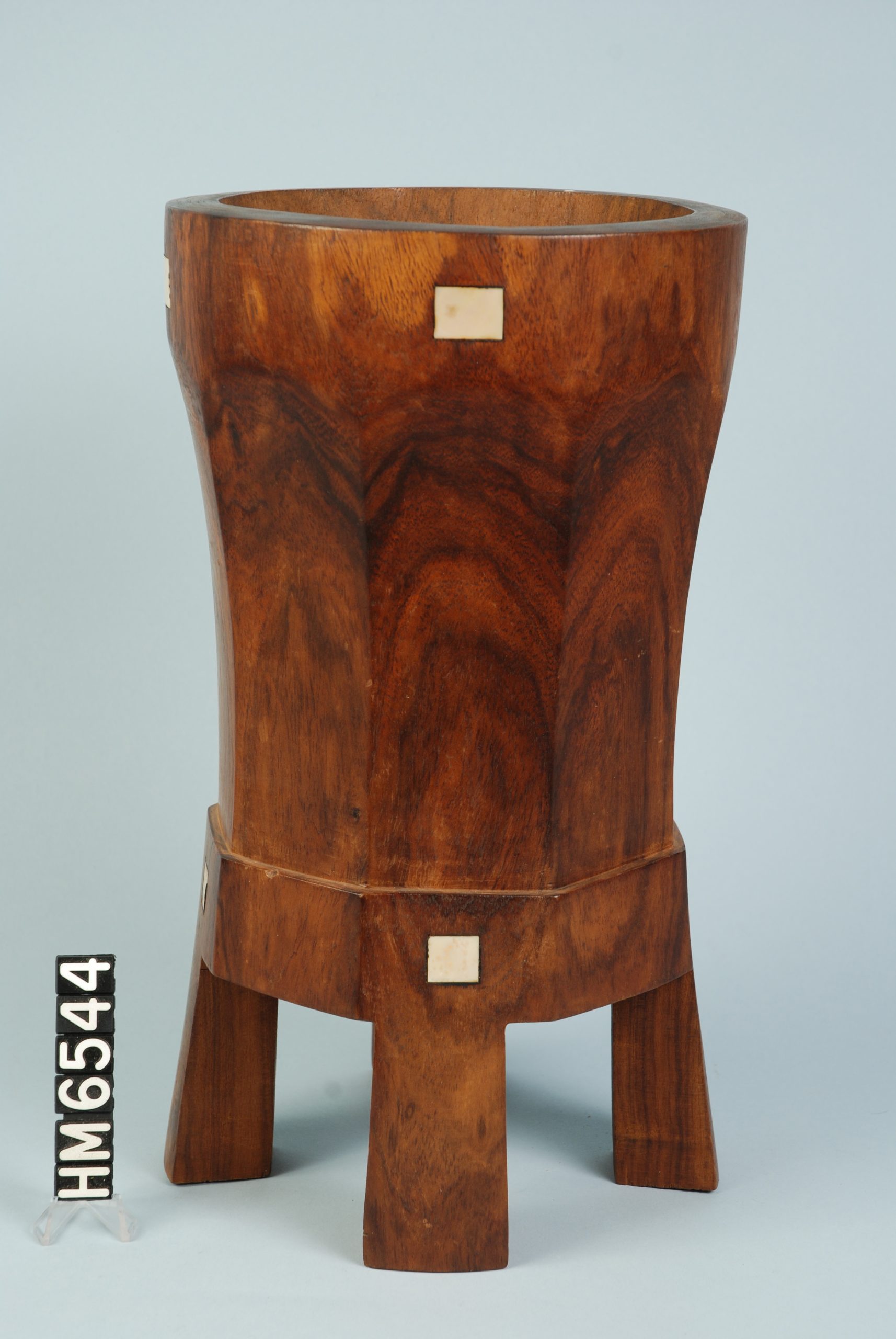 Image of a large wooden vessel with three visible legs and two inlaid white elements.