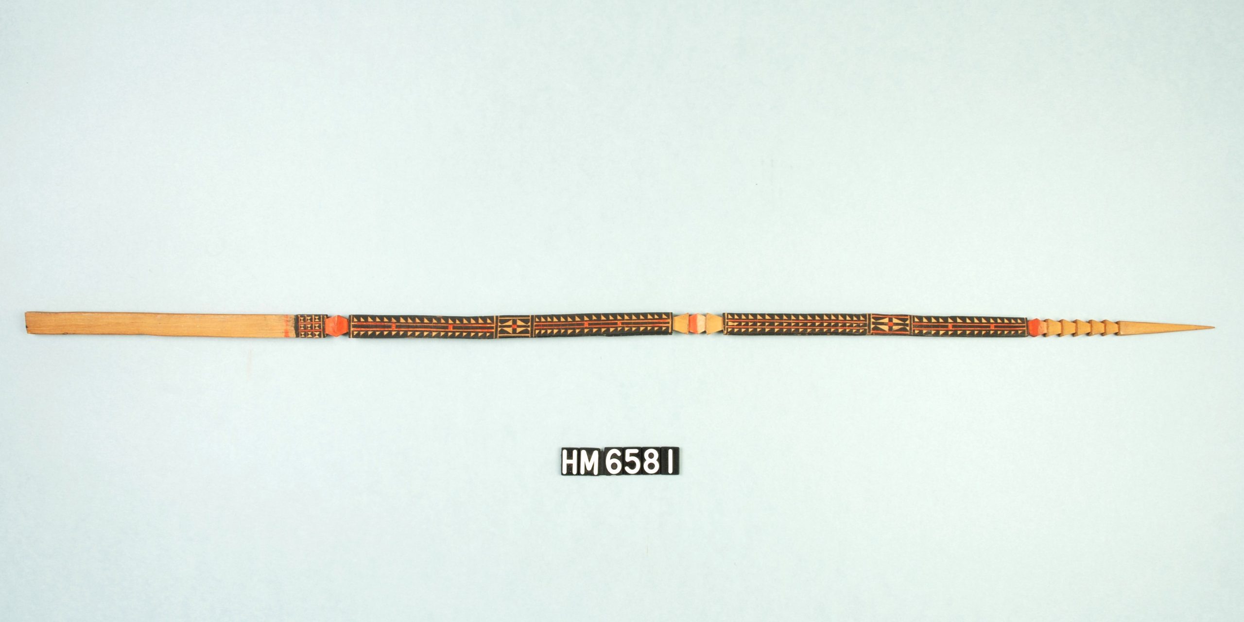 Image of stick, squared at the left end and pointed at the right. The center is decorated with carving and black paint.