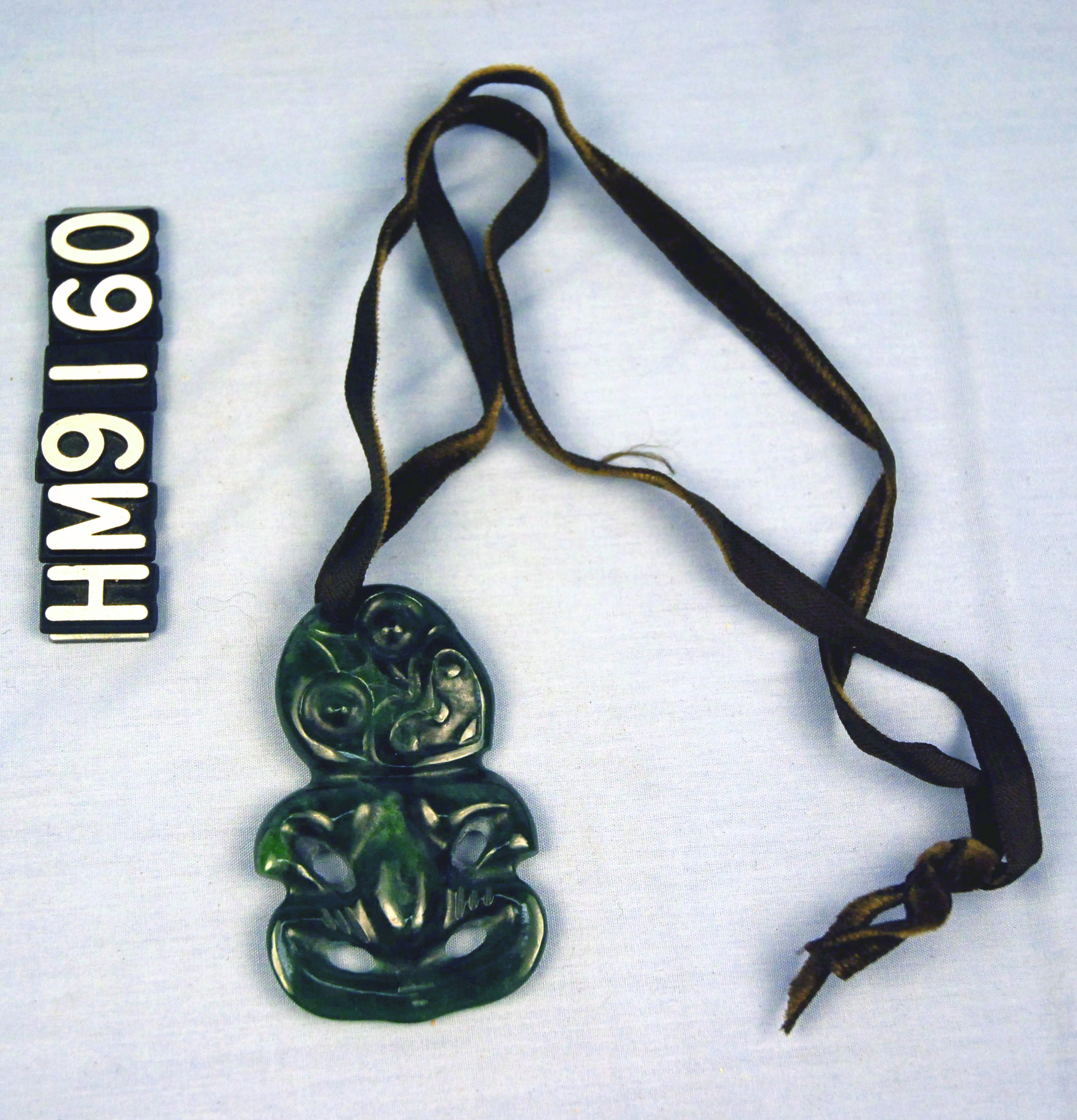 Image of a necklace made with a carved greenstone figure on a leather cord.