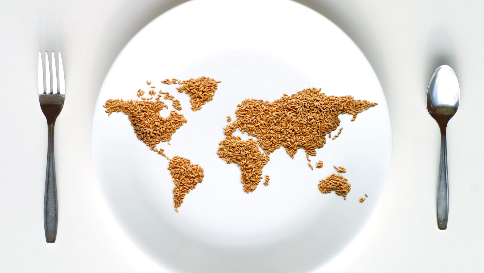 Map of the world made of grain on a plate, with a fork and spoon on either side