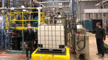 Employees stand in front of large processing equipment
