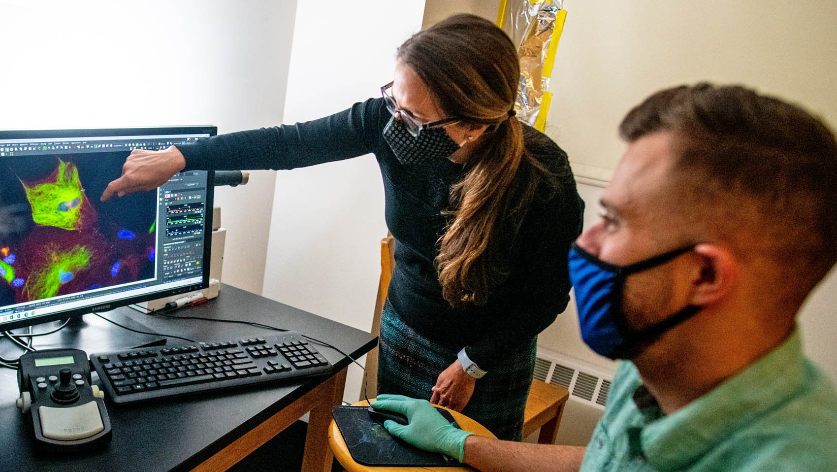 Melissa Maginnis points to a computer screen while a masked man looks on
