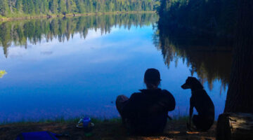 Michelle Moschkau sits on the edge of a lake with a dog
