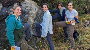 A photo of researchers standing outside next to a large rock