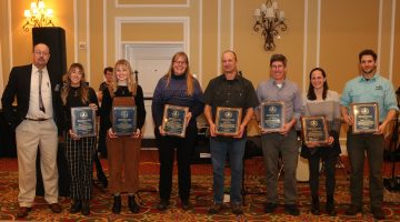 A group of people holding awards in a carpeted ballroom
