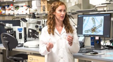 A woman in a lab coat in front of a monitor in a lab