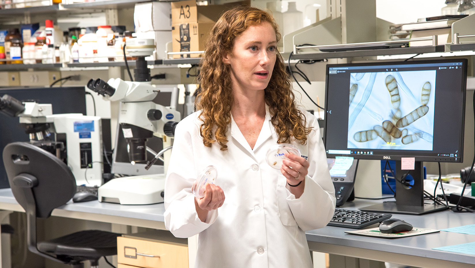 A woman in a lab coat in front of a monitor in a lab