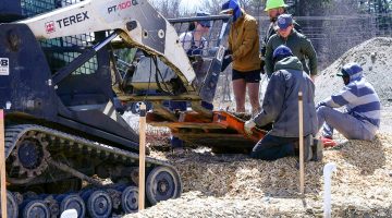 A group of people in hard hats watching a machine add a pallet of wild blueberries to the ground.