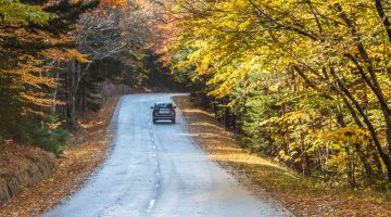 A photo of a car driving on a Maine road