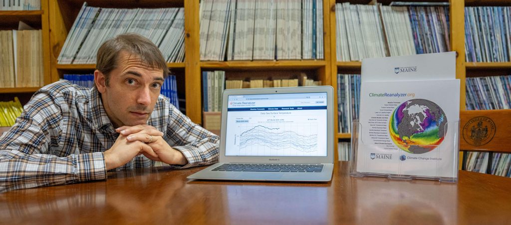 A photo of Sean Birkel sitting at a table next to a laptop that is open to the Climate Reanalyzer site