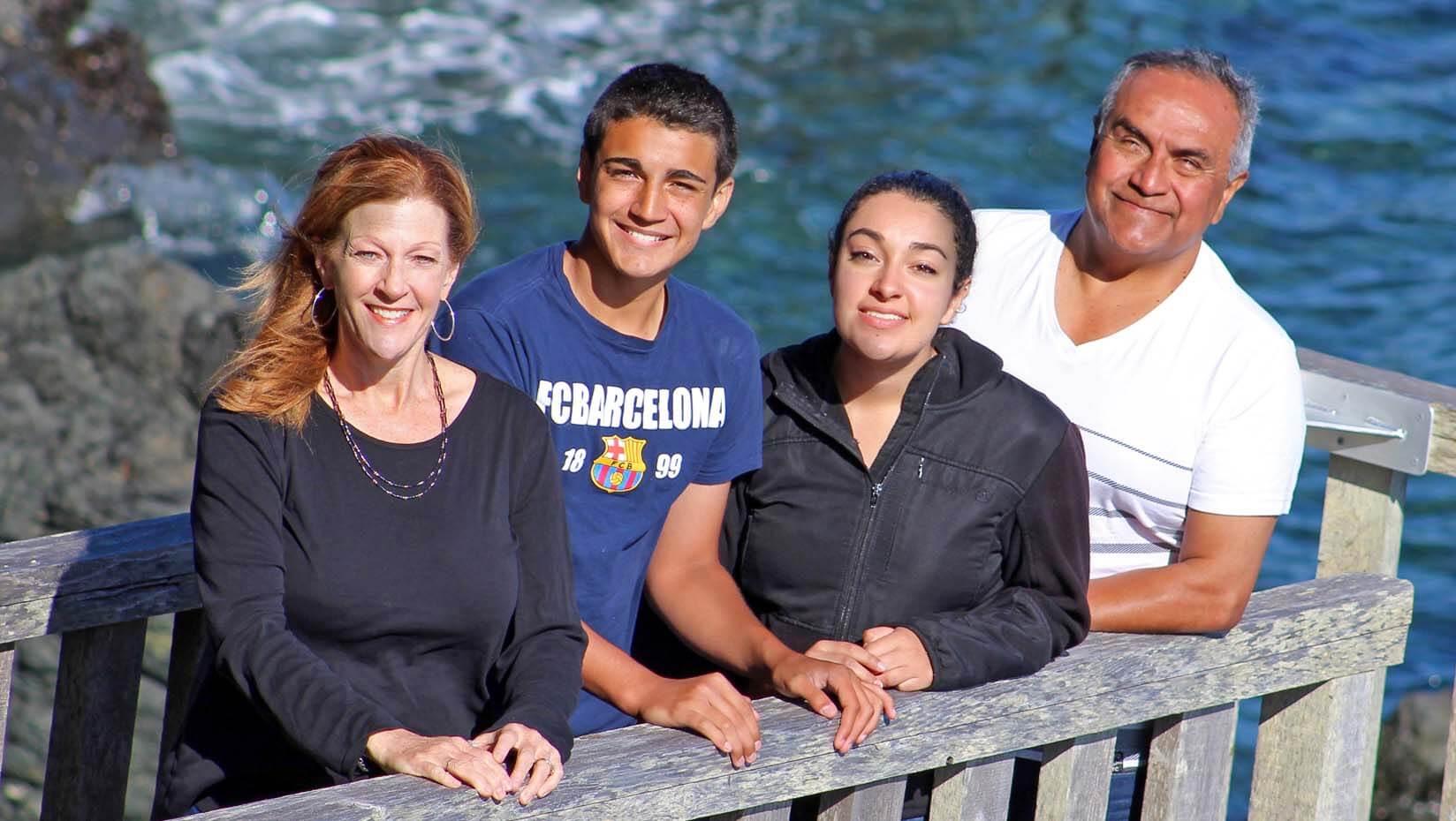 A photo of a family of four standing in front of water