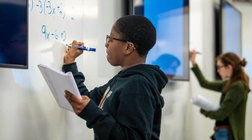 A photo of two students writing math equations on a white board