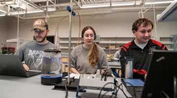 Photo of three people working in a lab, two of whom are using computers.