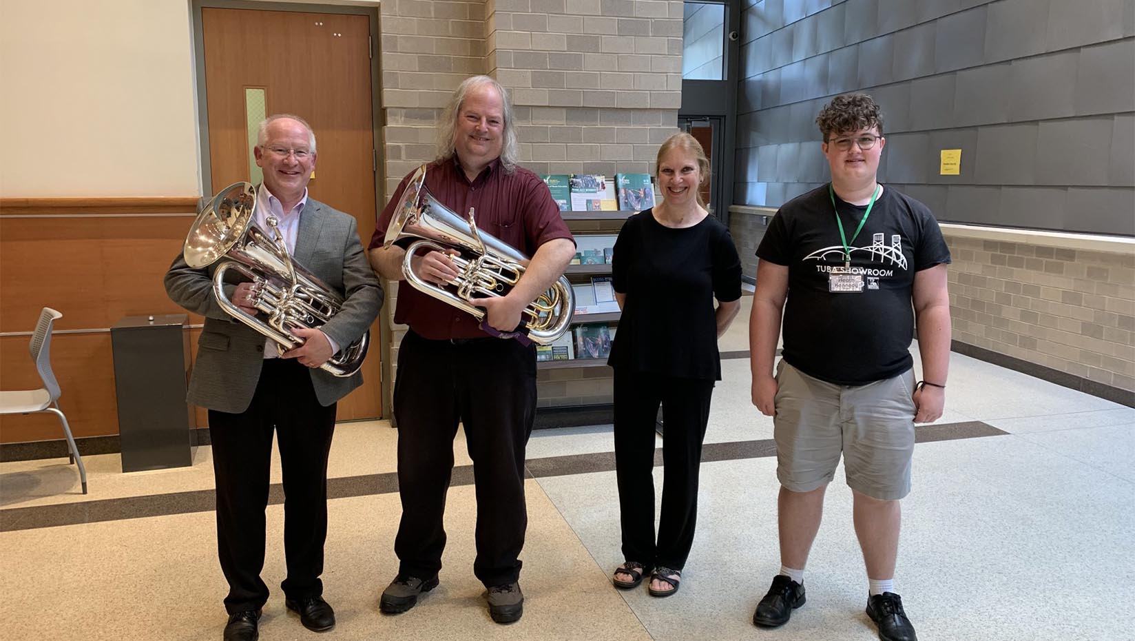 A photo of four people posing for a picture. Two people are holding tubas.