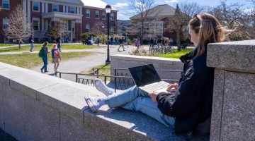 A photo of a student sitting on the front steps of Fogler Library in the spring