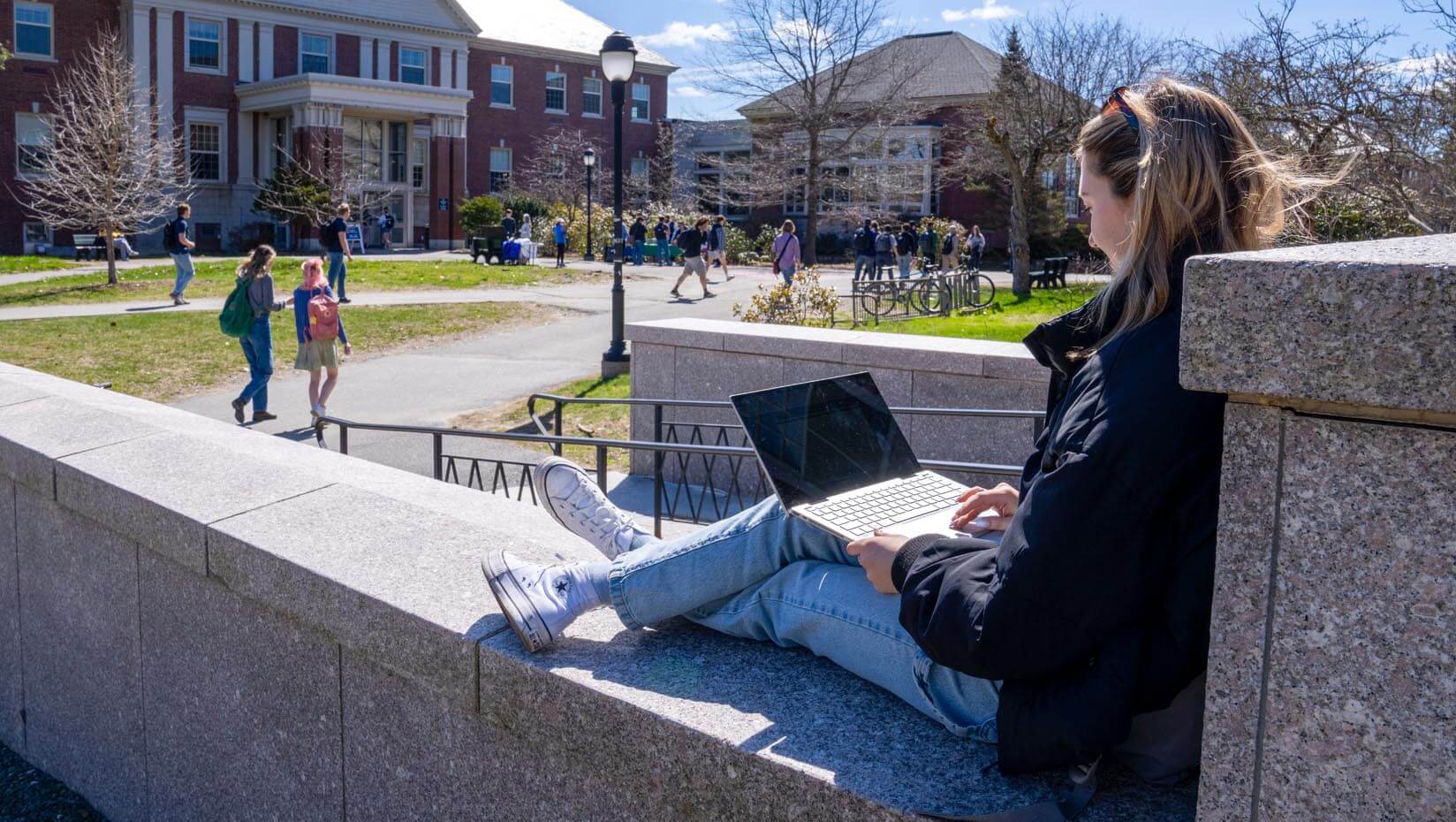 A photo of a student sitting on the front steps of Fogler Library in the spring