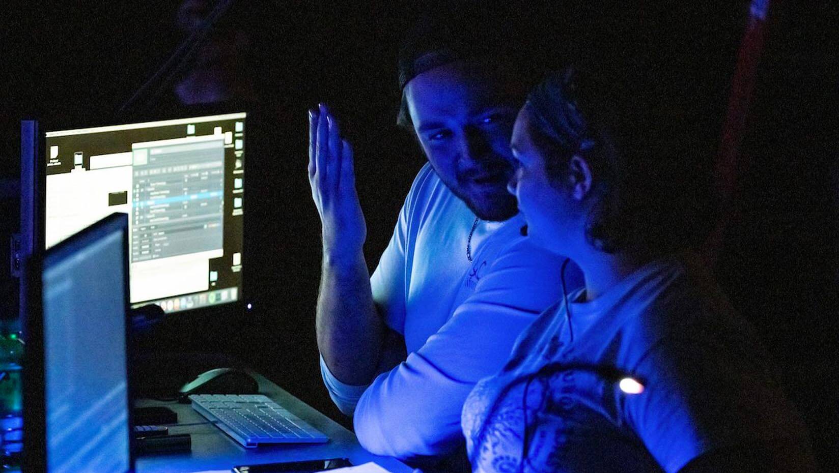 A photo of two people in front of computer screens