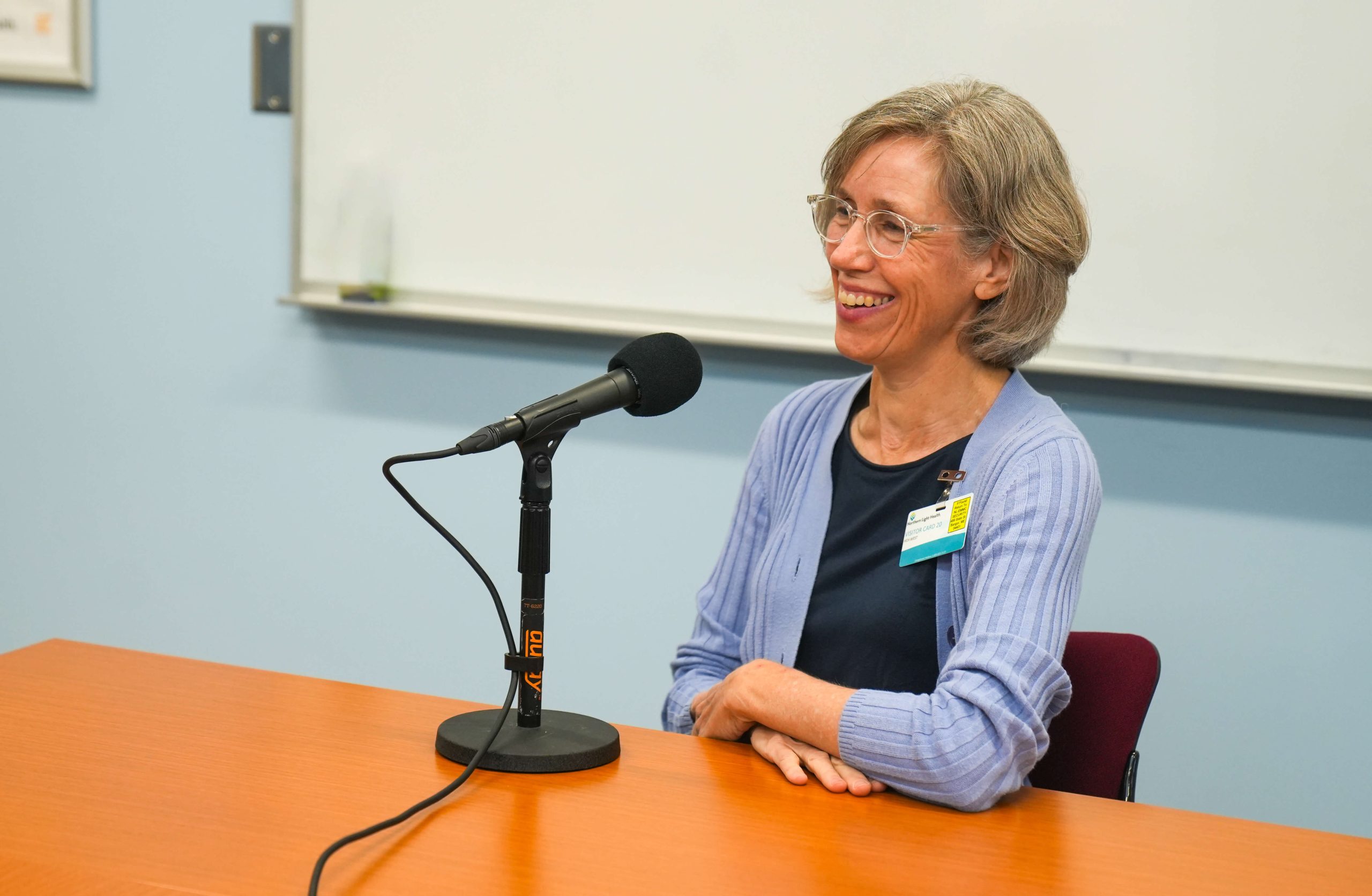 A photo of a woman sitting at a table next to a microphone.