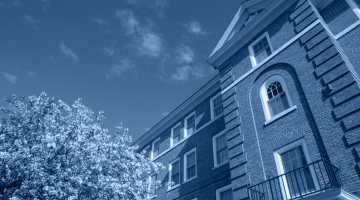 An image of a brick building on UMaine's campus with trees and flowers in front.