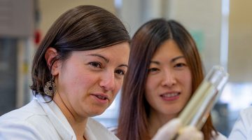 A researcher holds up a test tube as another researcher look on.
