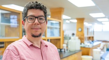 Onur Apul poses for portrait in lab with warm wood tones