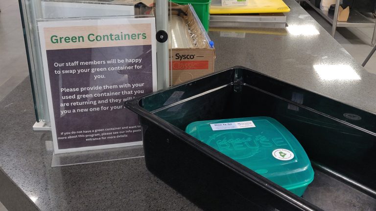 A green reusable takeout container with information regarding its use